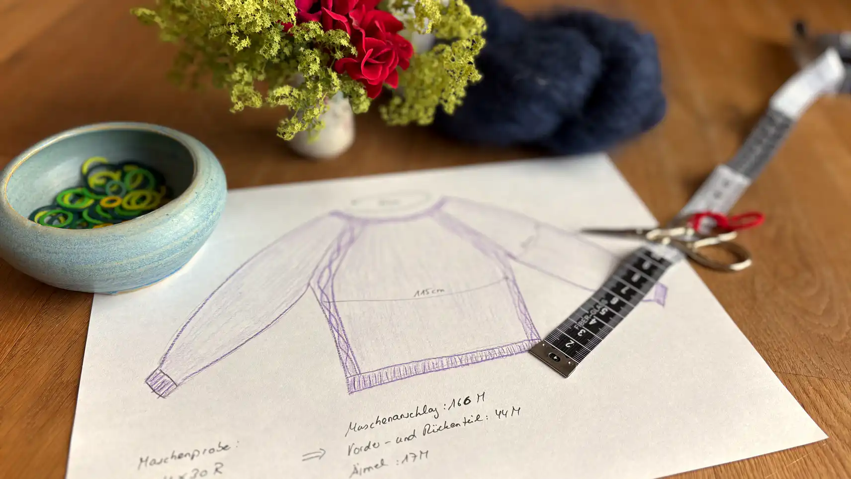 Entwurf eines Pullovers auf dem Papier mit Strickzubehör und Blumen