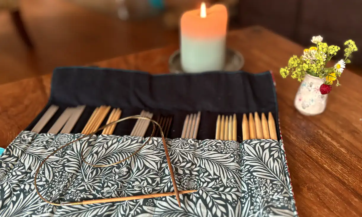 Stricknadeln in einer Mappe mit Kerze und Blumen